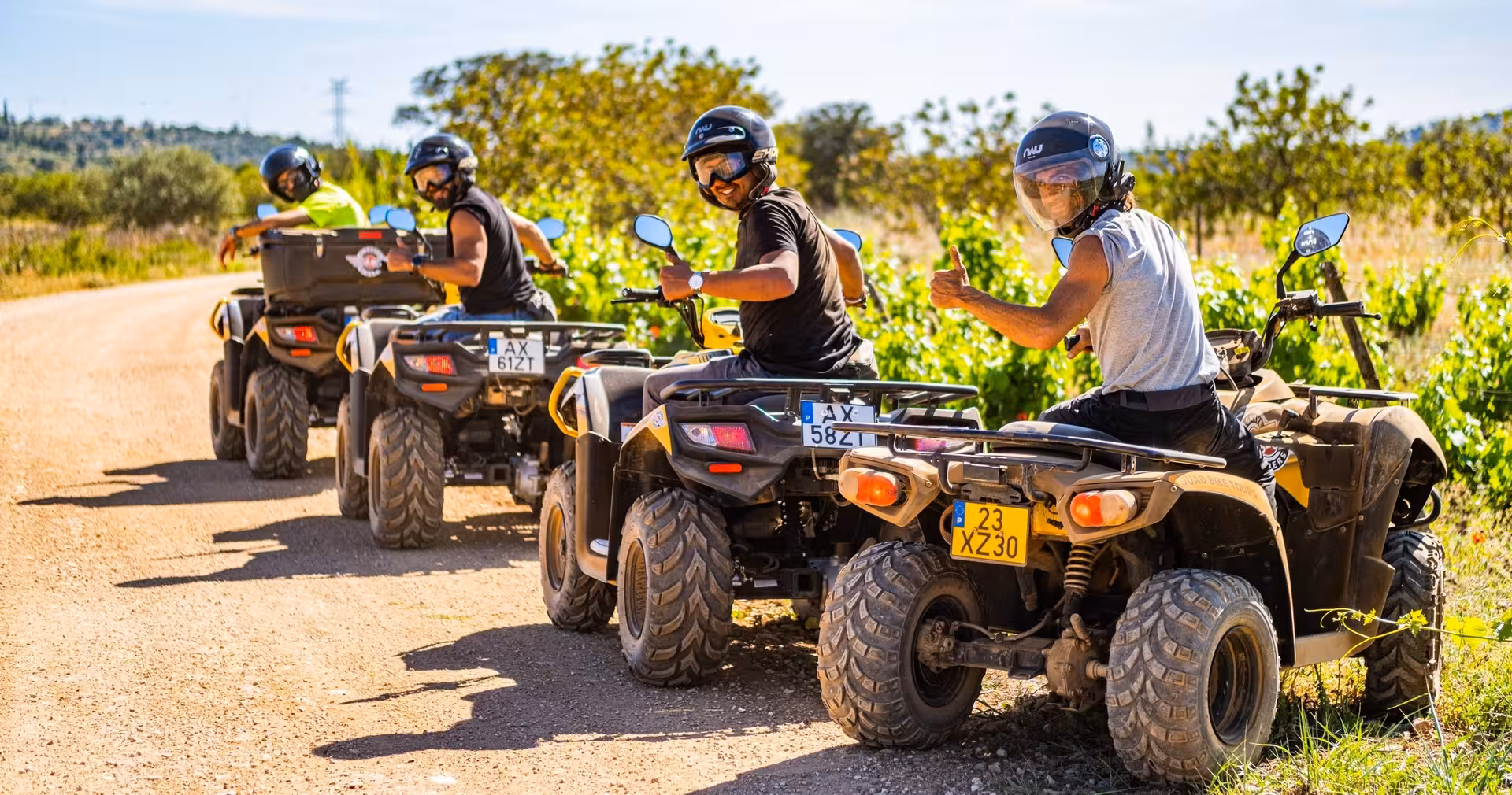 Happy friends on quad bikes posing with thumbs up during a sunny countryside ATV tour on a dirt road