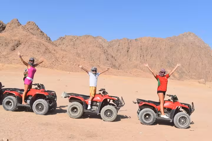 Friends on red ATVs with arms raised in Sinai Desert mountains during Sharm El Sheikh quad safari tour