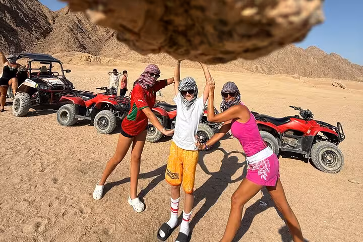 Friends pose by red quad bikes in Sinai desert on a private VIP Sharm El Sheikh ATV adventure tour