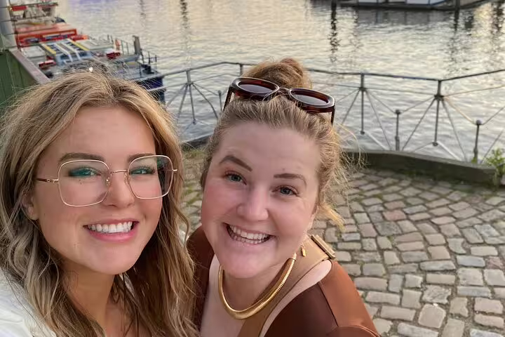 Two smiling women taking a selfie at Hamburg waterfront with cobblestone path and harbor in background