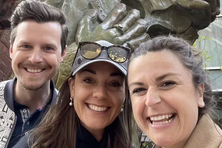 Three smiling friends posing for a selfie in front of a bronze sculpture during a Pittsburgh self-guided tour