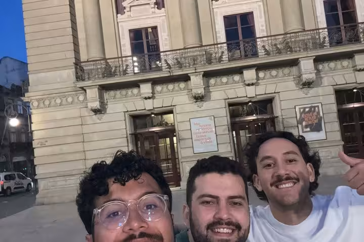 Three smiling men taking a selfie in front of a historic building in Porto Old Town at dusk