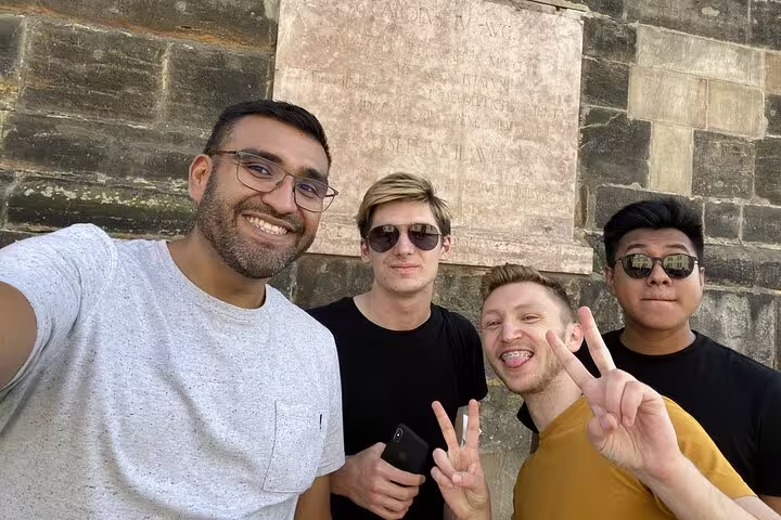 Four smiling men taking a selfie in front of a historic stone wall in Prague Old Town
