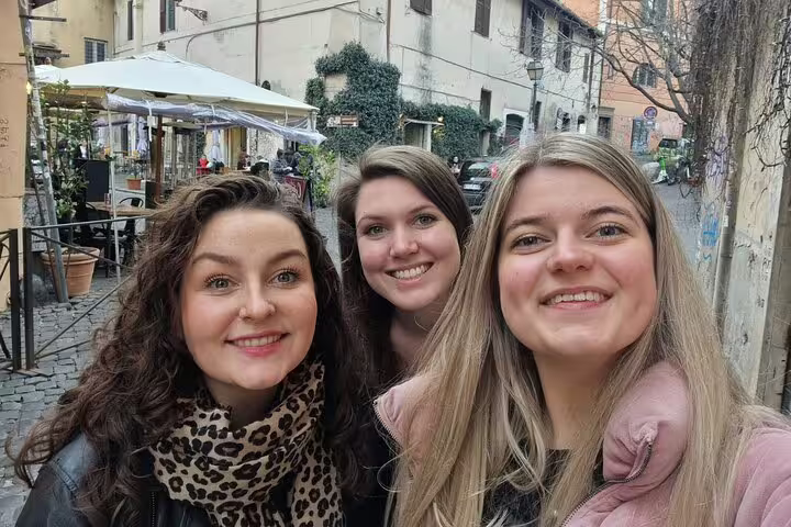 Three smiling women taking a selfie on a cobblestone street in Trastevere, Rome