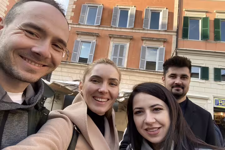 Four smiling friends taking a selfie in Trastevere Rome with colorful Italian buildings in background