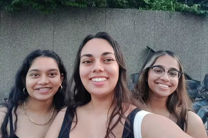 Three young women smiling together outdoors near a stone wall in Ottawa