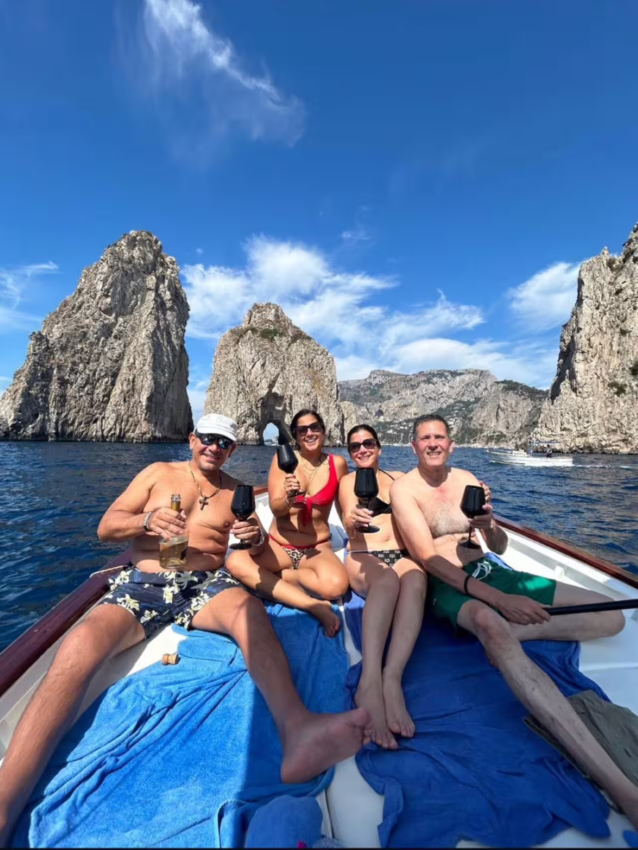Friends toast with wine on a shared Capri boat tour by the Faraglioni rocks, enjoying a full-day cruise in Italy