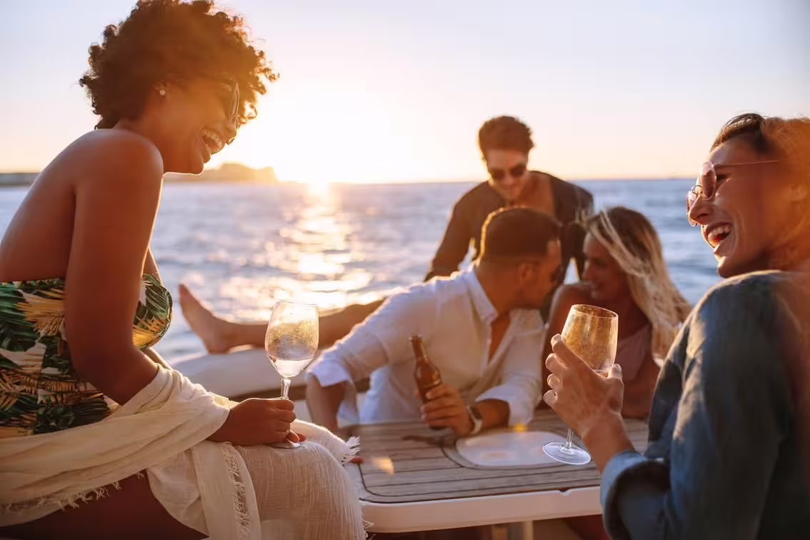 Friends toasting wine on a sunset boat cruise during Festa di Sant’Anna with views of Ischia coastline in summer