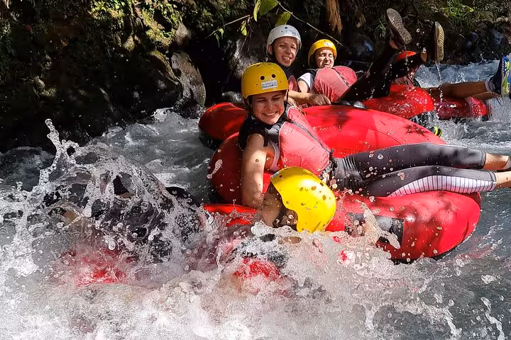 Group of friends laughing and tubing down Rio Celeste, surrounded by lush greenery and rushing water.