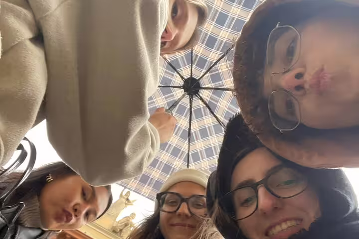 Group of friends huddled under a plaid umbrella on a walking tour in Bologna old town