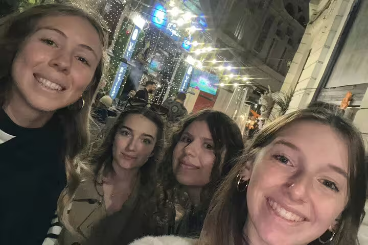 Four smiling women taking a selfie on a lively lit street in Bucharest Old Town at night