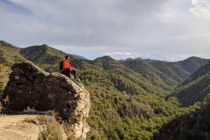 Hiker enjoying panoramic mountain views on a rocky ledge during the Frigiliana hike from Málaga.