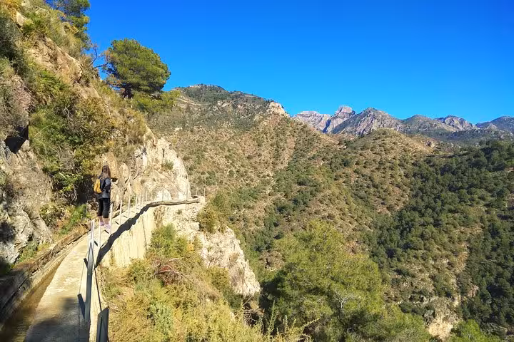 Hiker traverses a narrow mountain trail with stunning views of the rugged landscape near Frigiliana, perfect for nature lovers.