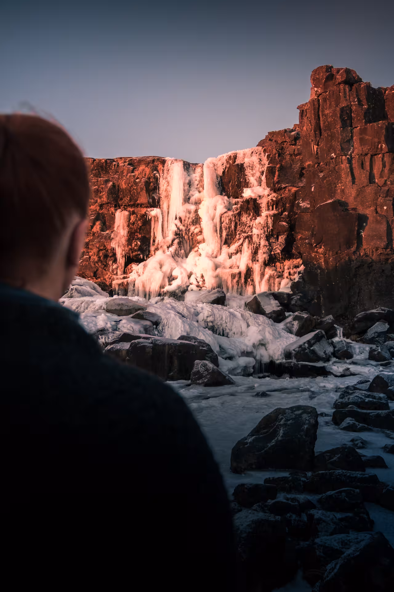 Person viewing a frozen waterfall on Iceland's Golden Circle tour at sunset