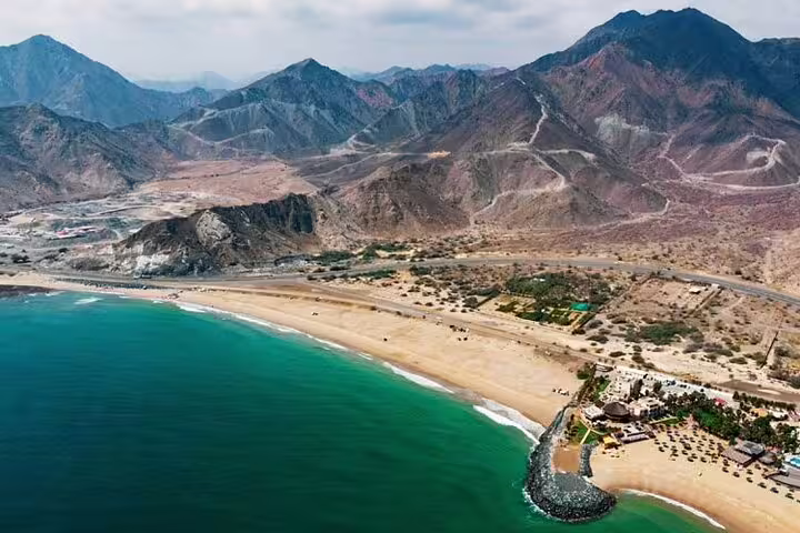 Aerial view of Fujairah's coastline with turquoise waters and rugged mountains, ideal for nature and heritage tours.