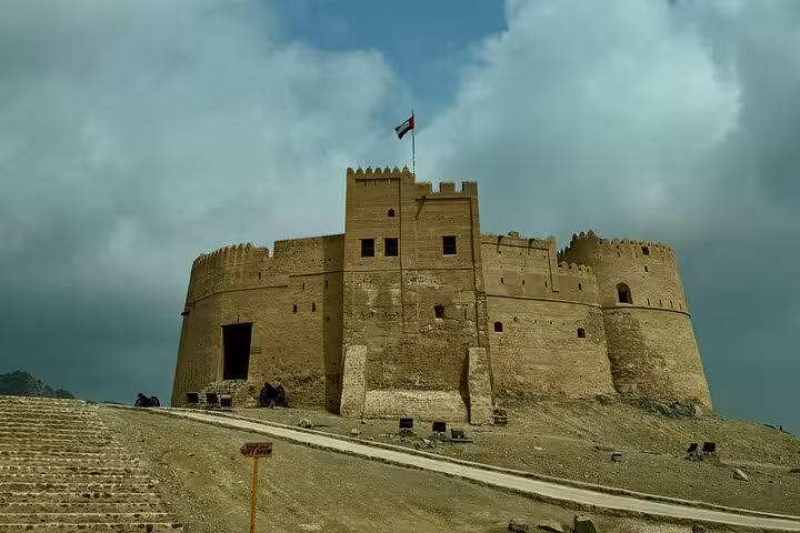 Fujairah Fort with UAE flag under dramatic clouds on Fujairah City Khorfakkan tour, historic museum landmark