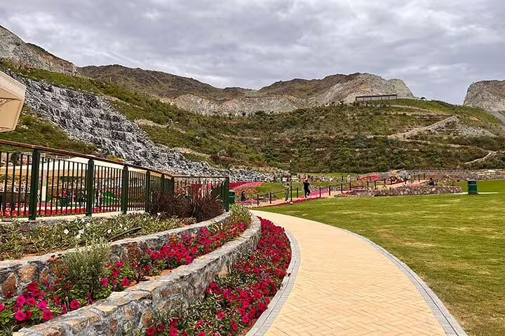 Beautiful garden path lined with vibrant flowers and stone terraces leading to the hills of Fujairah.