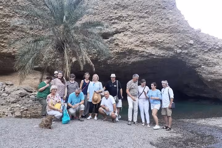 Visitors at rocky cave and palm oasis during Fujairah Khorfakkan mountains safari sightseeing tour in UAE