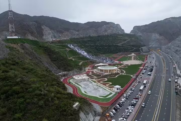 Aerial view of a landscaped park in Fujairah with lush greenery, winding pathways, and a busy adjacent highway.
