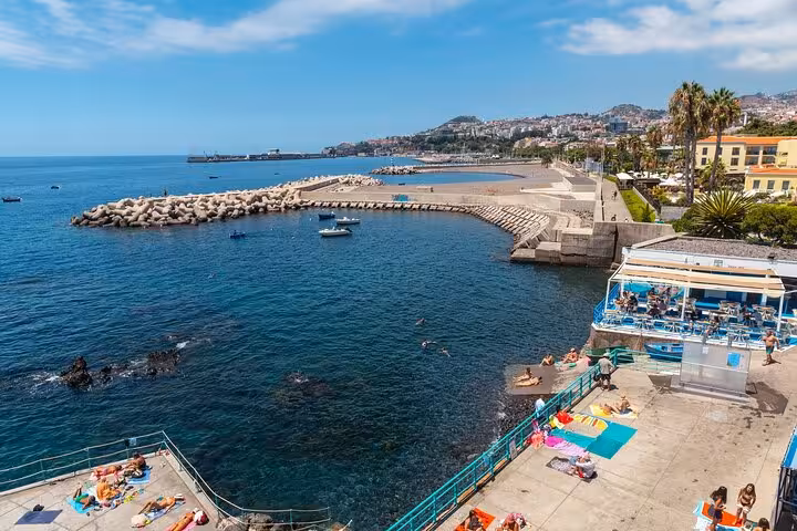 Scenic Funchal coastline with sunbathers and clear blue waters, showcasing vibrant beach life and stunning ocean views.