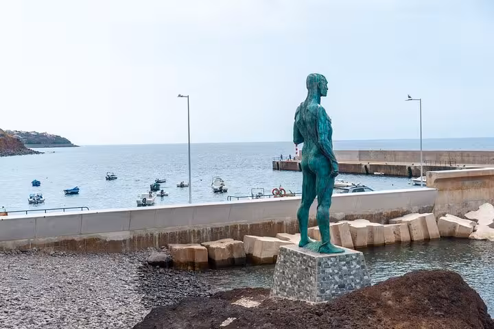Bronze statue overlooking the serene harbor in Funchal, Madeira, with boats dotting the calm sea, ideal for a city walk.