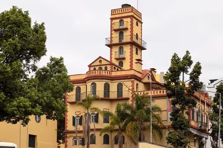 Historic yellow and red building with tower in Funchal, Madeira, surrounded by palm and green trees