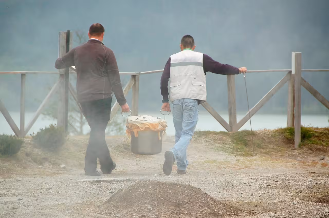 Guides carry a steaming pot of traditional Furnas cozido from geothermal ground on a full day van lake tour in the Azores