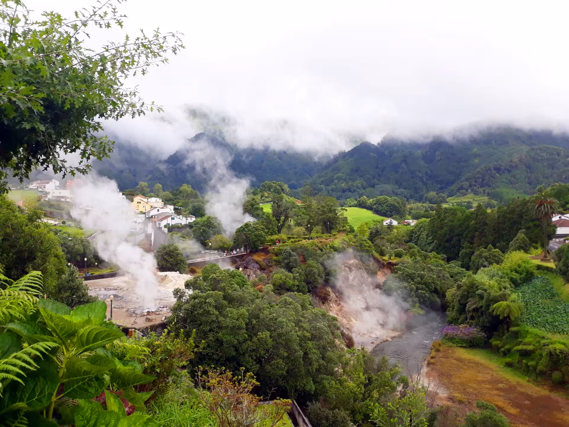 Panoramic view of Furnas Valley with steaming geothermal vents, lush green hills and village houses in São Miguel