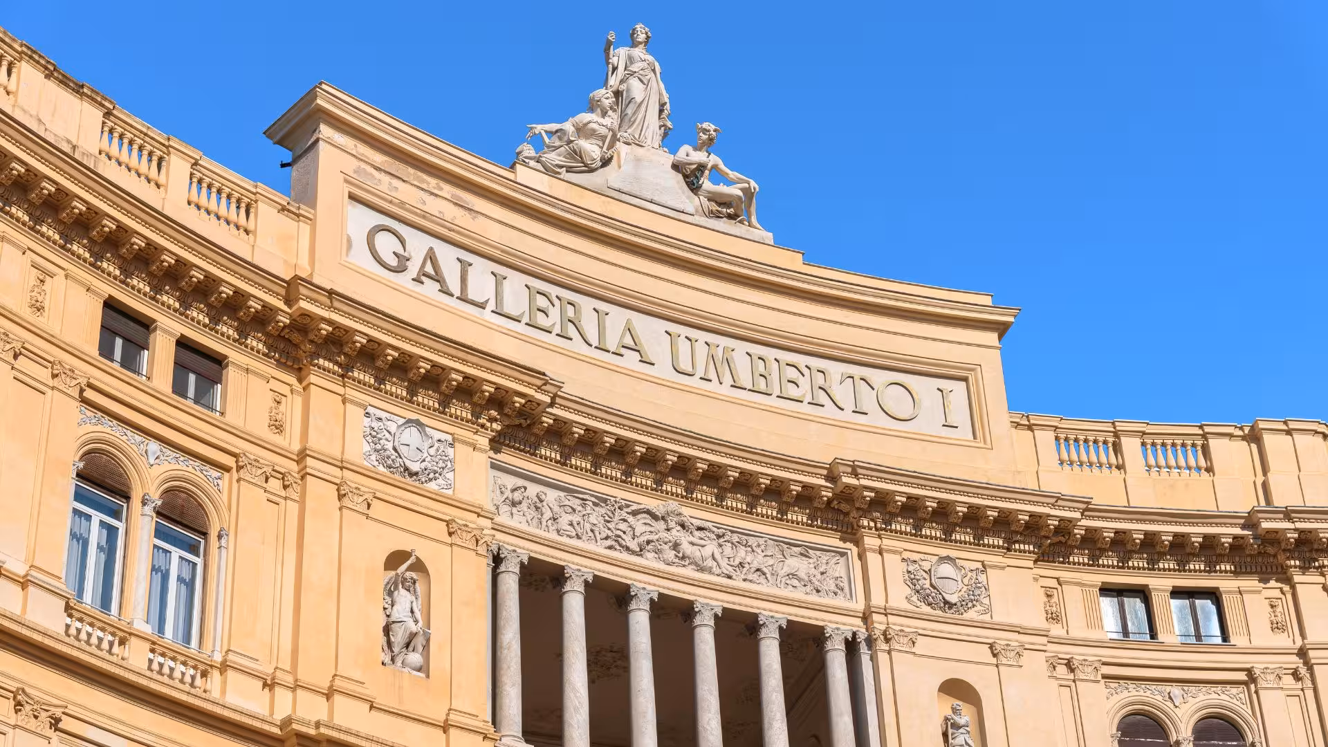 The elegant facade of Galleria Umberto I in Naples, showcasing intricate architectural details and sculptures.