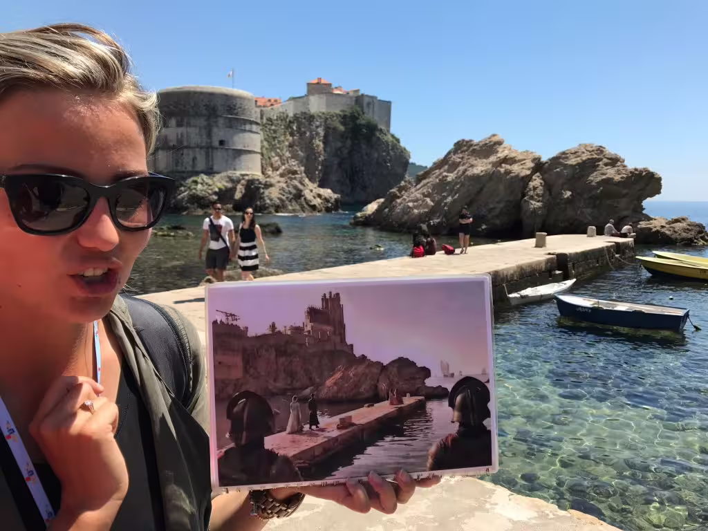 Traveler holds Game of Thrones still at Dubrovnik harbor, comparing Kings Landing filming spots on walking tour