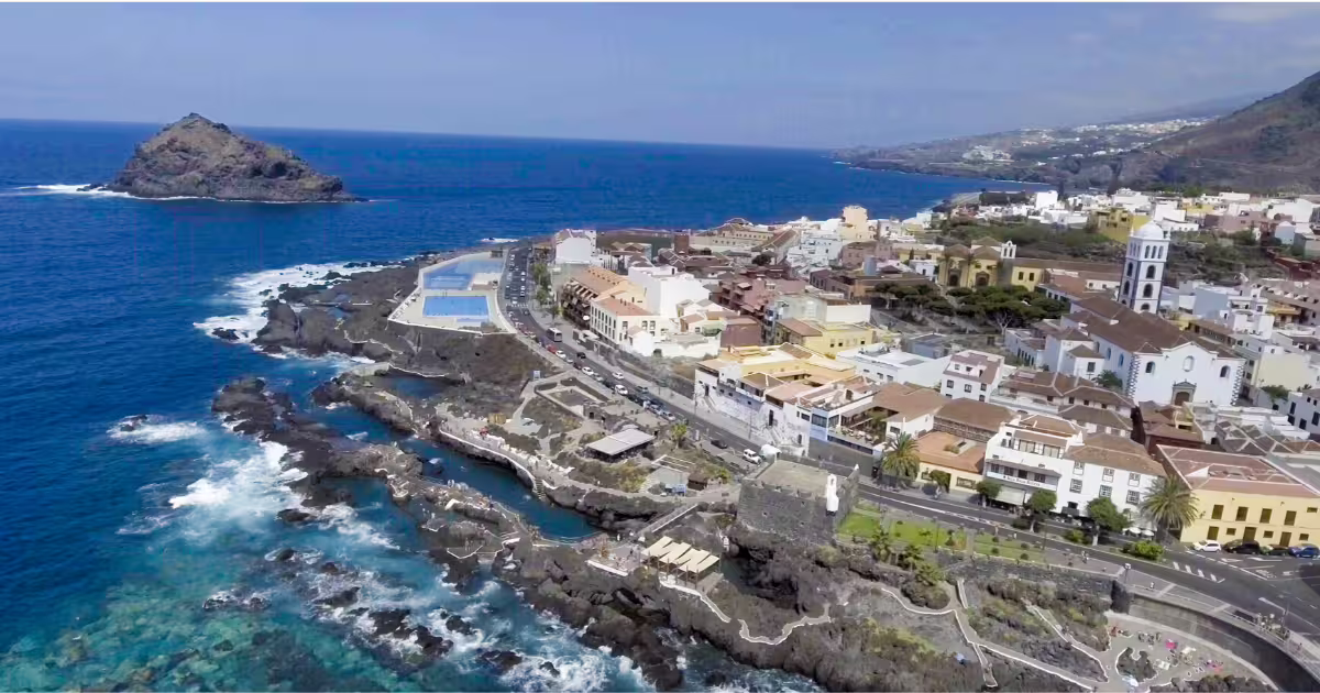 Aerial view of Garachico's rugged coastline, vibrant town, and natural pools against the backdrop of the Atlantic Ocean.