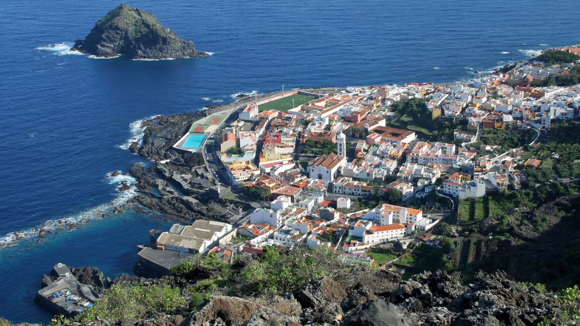 Aerial view of Garachico's coastal town with vibrant buildings, ocean, and natural pools in Tenerife, Canary Islands.