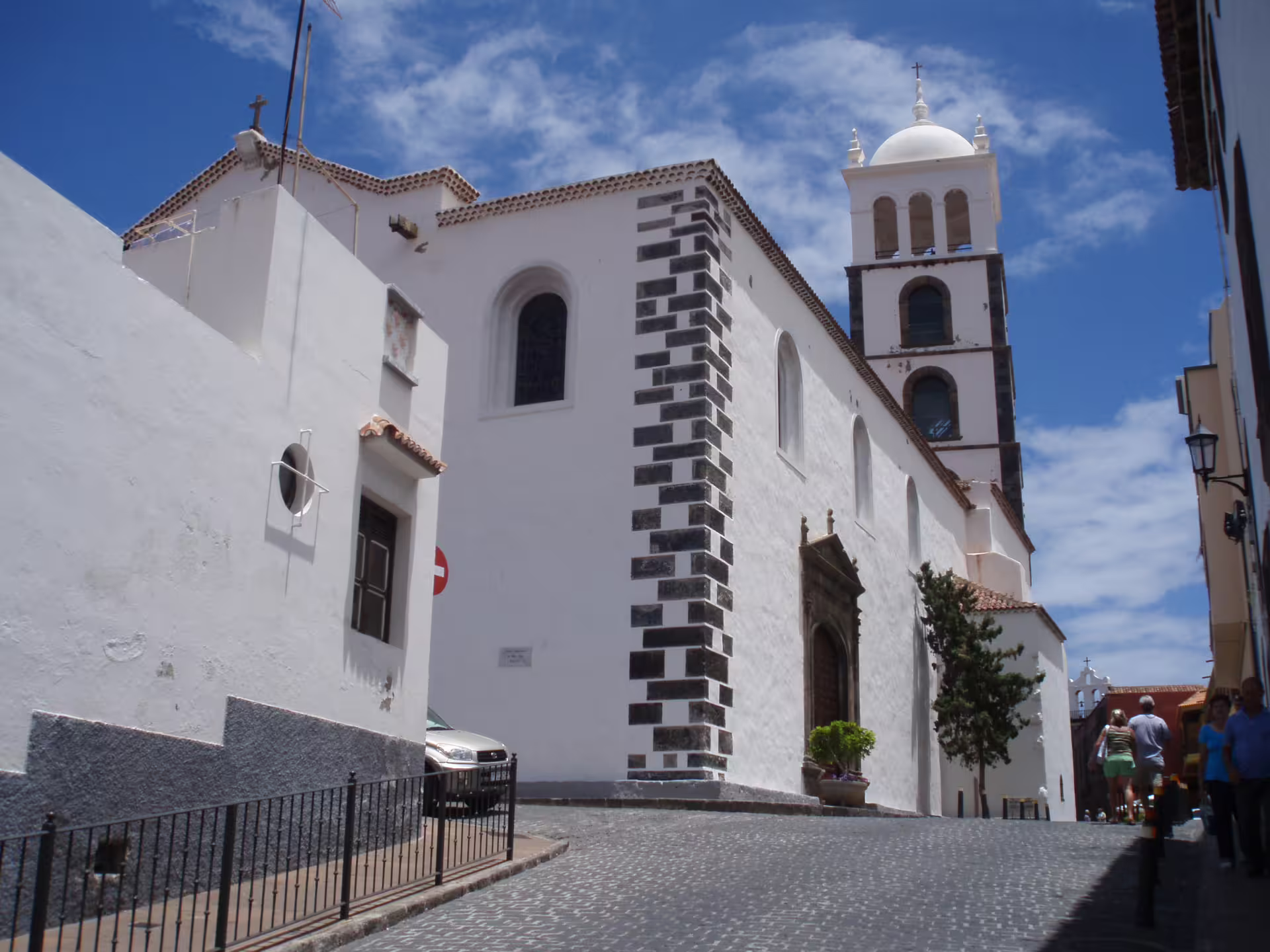 Charming white church with a bell tower on a cobblestone street in Garachico, Tenerife, under a vibrant blue sky.