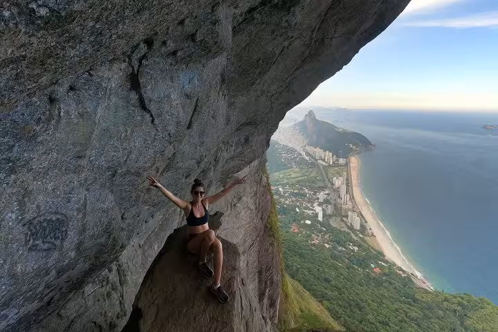 Adventurer posing on Garganta do Céu's edge with stunning beach and city views at Pedra da Gávea hike in Rio.