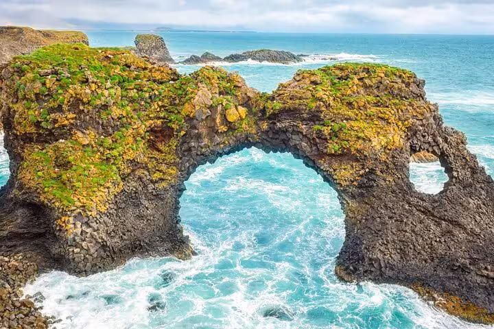 Natural rock arch with moss over turquoise ocean waves on Snaefellsnes Peninsula, Iceland