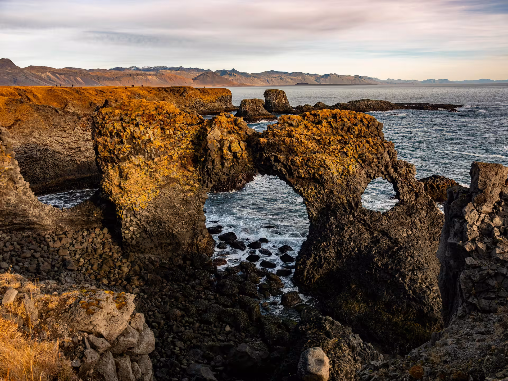 Gatklettur rock arch on Snaefellsnes Peninsula coastline with ocean waves and mountains beyond