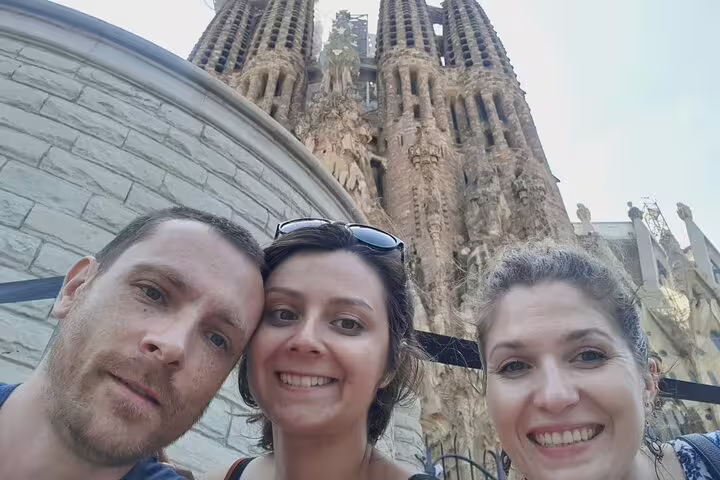 Three tourists smiling in selfie in front of Sagrada Família towers in Barcelona