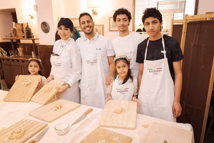 Family enjoying a gelato and fettuccine pasta cooking class in Rome's Piazza Navona, showcasing wooden boards and dough.