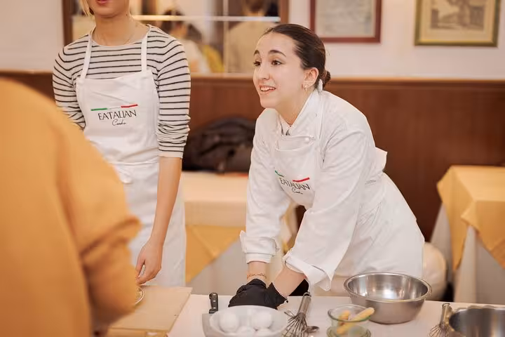 Instructor guiding participants in a gelato and fettuccine pasta cooking class in Rome, with bowls and eggs on the table.