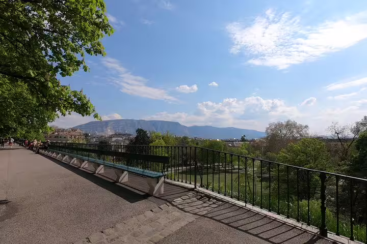 Scenic walkway with iron railing overlooking Geneva park and mountain backdrop on a sunny day