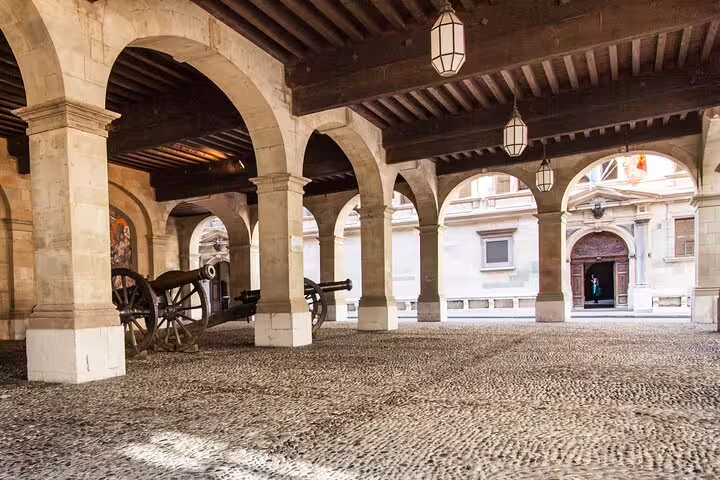 Historic Geneva arcade with stone arches, wooden ceiling, and antique cannons on cobblestone courtyard