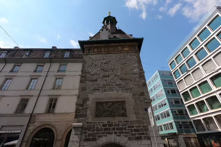Historic stone clock tower in Geneva old town between modern and classic buildings under blue sky