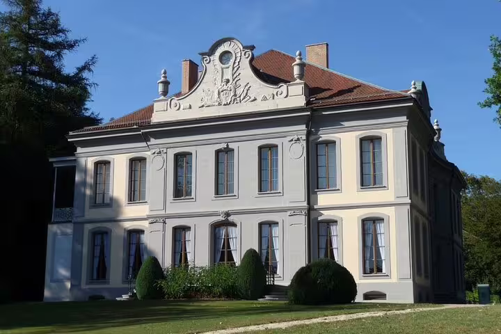 Elegant French-style château with ornate facade, red roof, and manicured gardens under blue sky