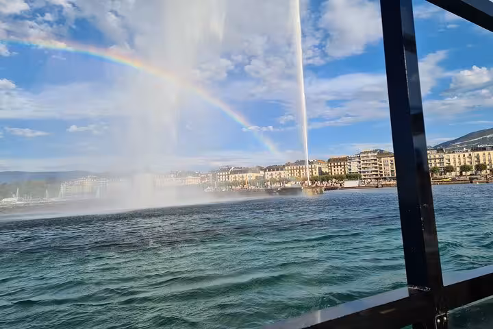 Vibrant rainbow over Lake Geneva with Jet d'Eau fountain and city skyline in the distance.