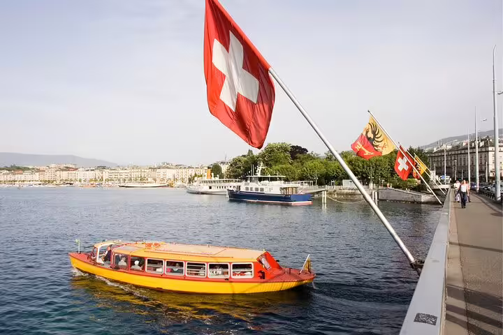 Swiss flags over Lake Geneva promenade with yellow boat, ideal stop on a Geneva scavenger hunt self-guided tour