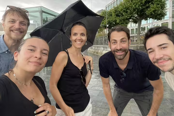 Group of five smiling friends posing for selfie outdoors in Geneva with black umbrella on cloudy day