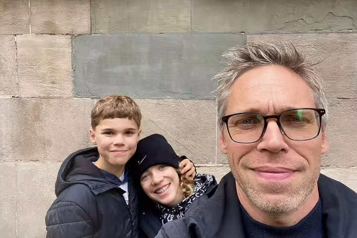 Man with two children posing for selfie in front of stone wall during Geneva walking tour