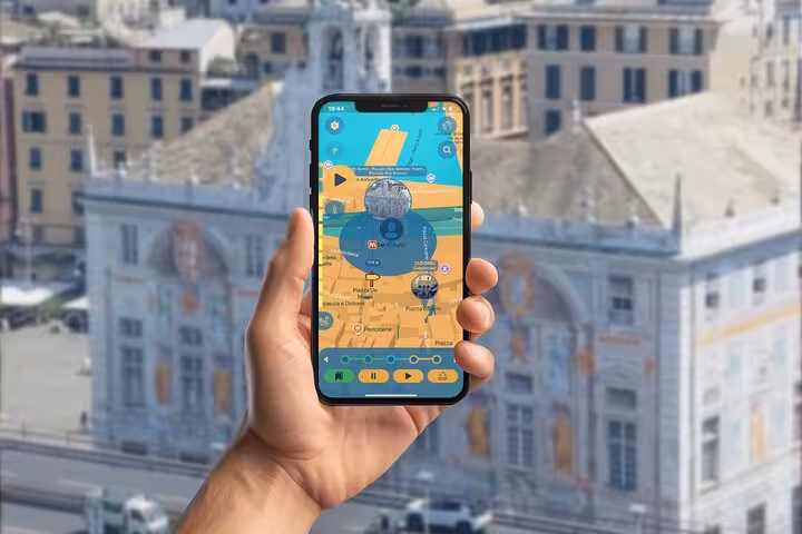 Hand holding smartphone displaying GPS self-guided tour map of Genoa city center with historic buildings in background