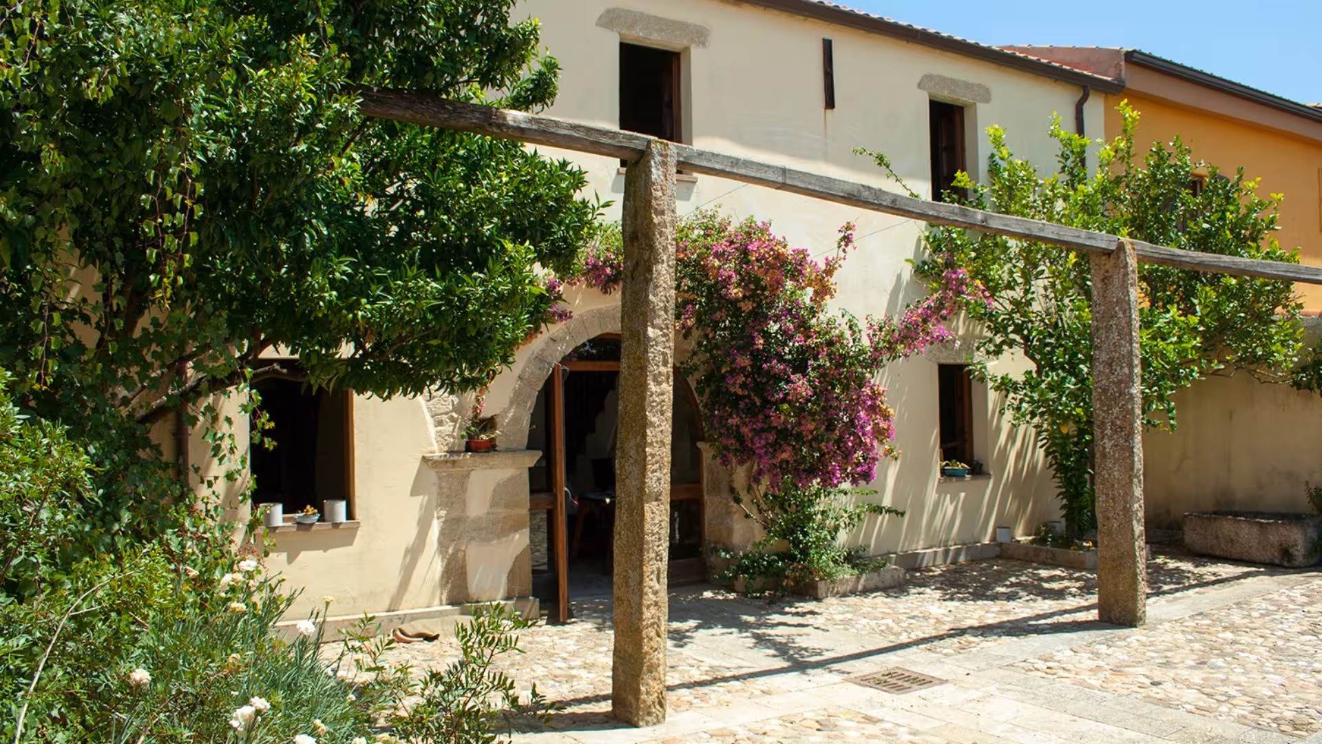 Charming rustic building surrounded by lush greenery and vibrant flowers in Giara Park, Genoni.