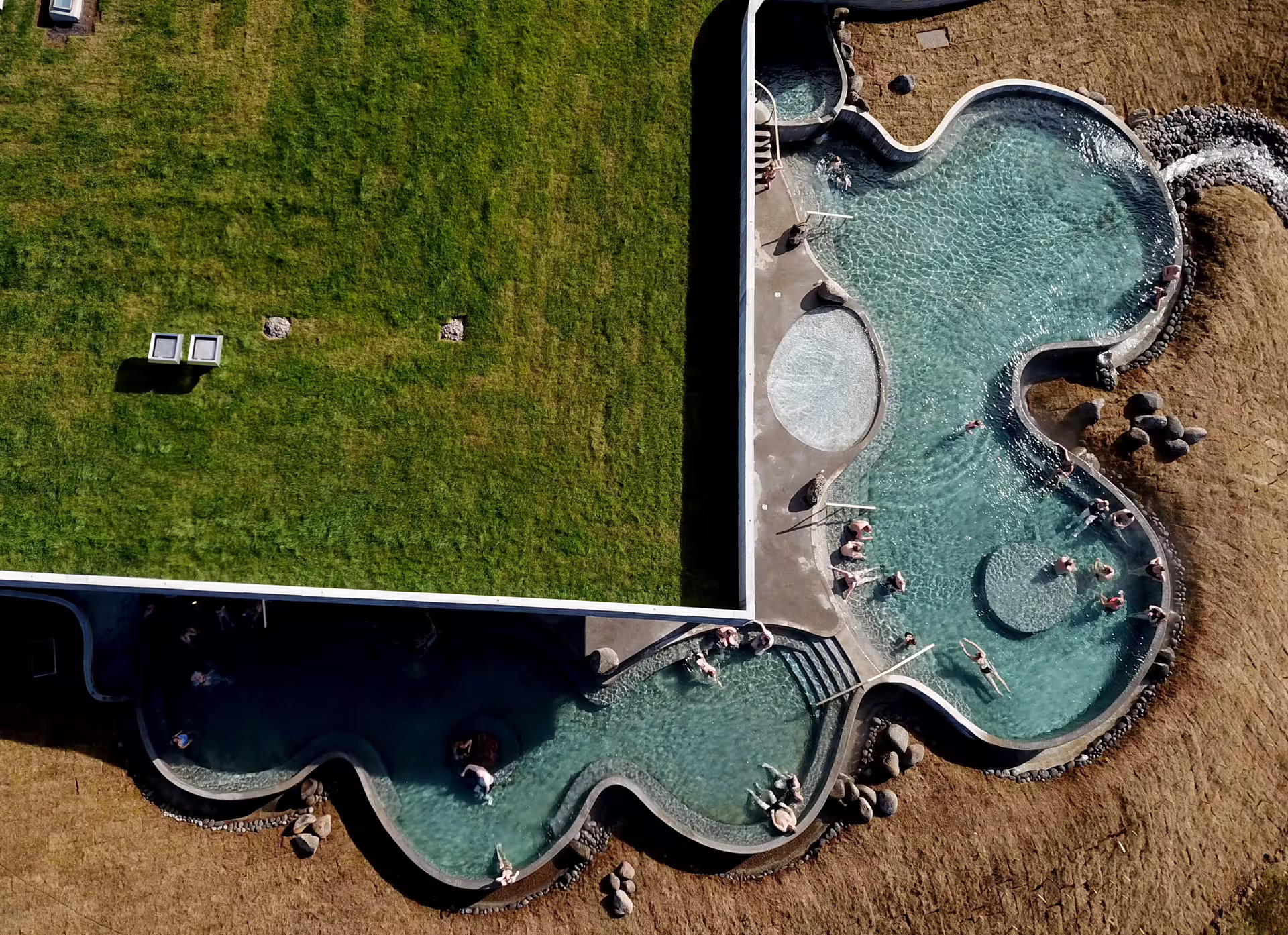 Aerial view of Geosea geothermal sea baths with wavy pools and bathers on Iceland coastline